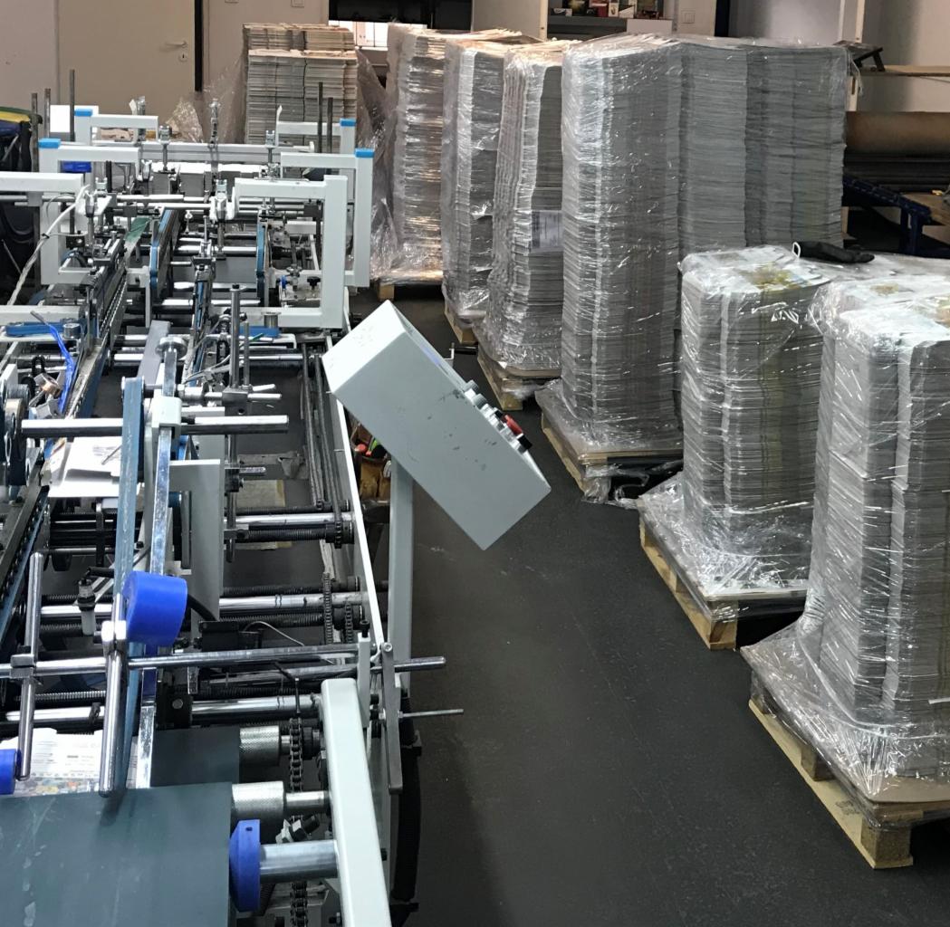 Automatyczna linia introligatorska w Chełmku, z widocznymi stosami gotowych, zapakowanych produktów na paletach w tle.