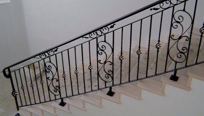 Kuta balustrada schodowa w kolorze czarnym z dekoracyjnymi elementami w kształcie spiral i liści, zamontowana na jasnych, kamiennych schodach.