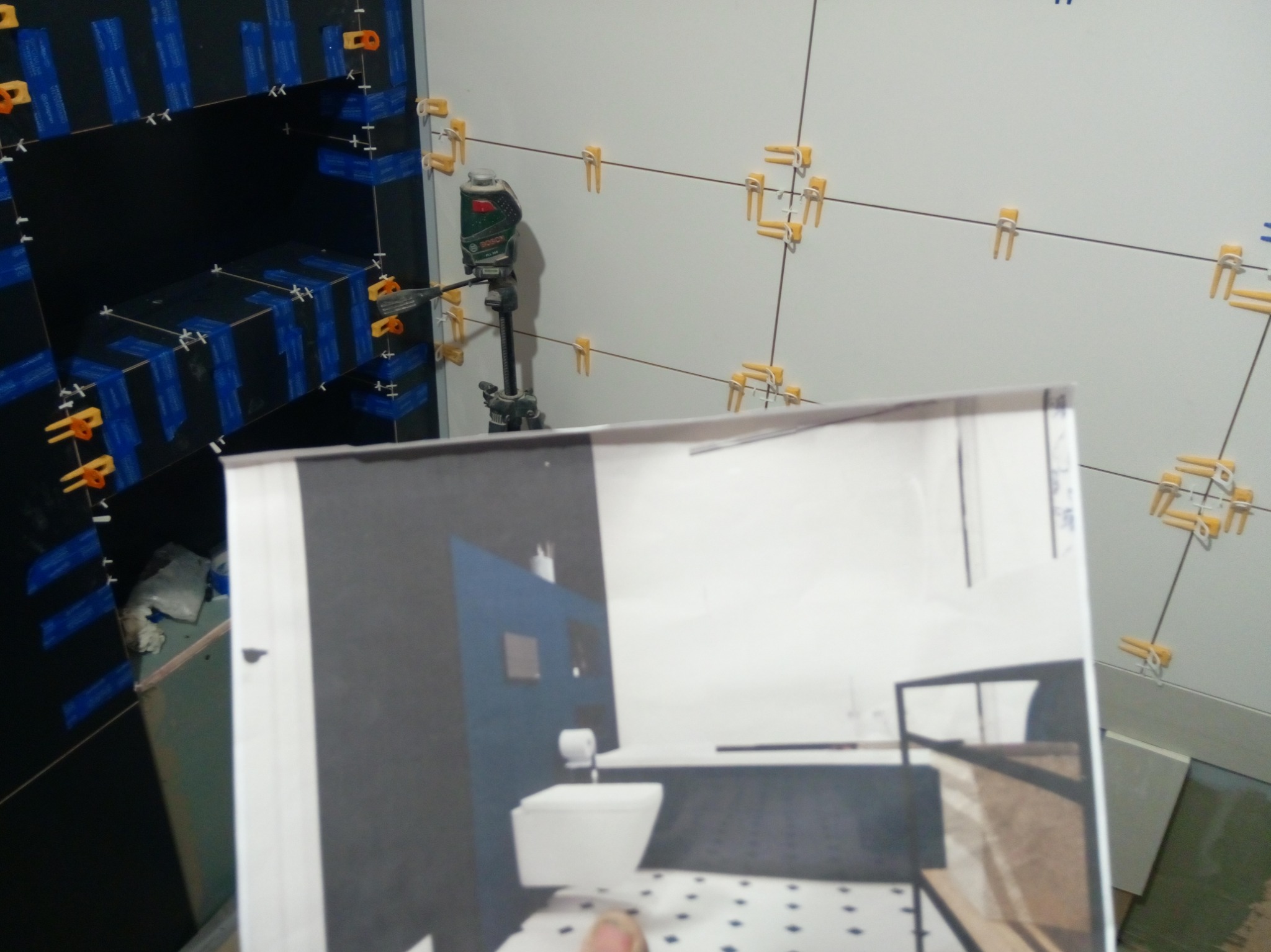 Układanie płytek w łazience, widoczny laser krzyżowy, fragment planu łazienki w dłoni