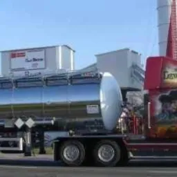 Czerwona ciężarówka z chromowaną cysterną i malowidłami na kabinie, zaparkowana na tle silosów.