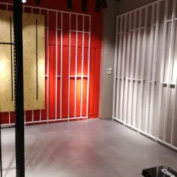 Pusta przestrzeń biurowa z szarą podłogą, czerwonymi i białymi ścianami z pionowymi listwami oraz czarnym systemem oświetlenia sufitowego