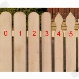 Sześć surowych, drewnianych sztachet ogrodzeniowych o różnych kształtach górnej krawędzi, oznaczonych cyframi od 0 do 5, na tle zieleni i fragmentu muru z cegły.