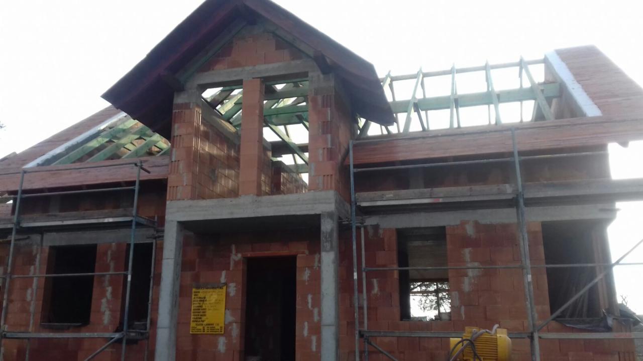 Budynek w stanie surowym otwartym, w trakcie budowy, widoczne rusztowania i żółty agregat prądotwórczy na pierwszym planie.