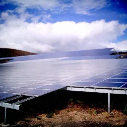 Rozległa farma paneli słonecznych na wzgórzu pod błękitnym niebem z białymi chmurami, widok z dołu z metalową konstrukcją wsporczą w pierwszym planie.