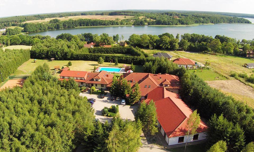 Widok z lotu ptaka na ośrodek wypoczynkowy w Silnowie z basenem, otoczony zielenią i jeziorem w tle.
