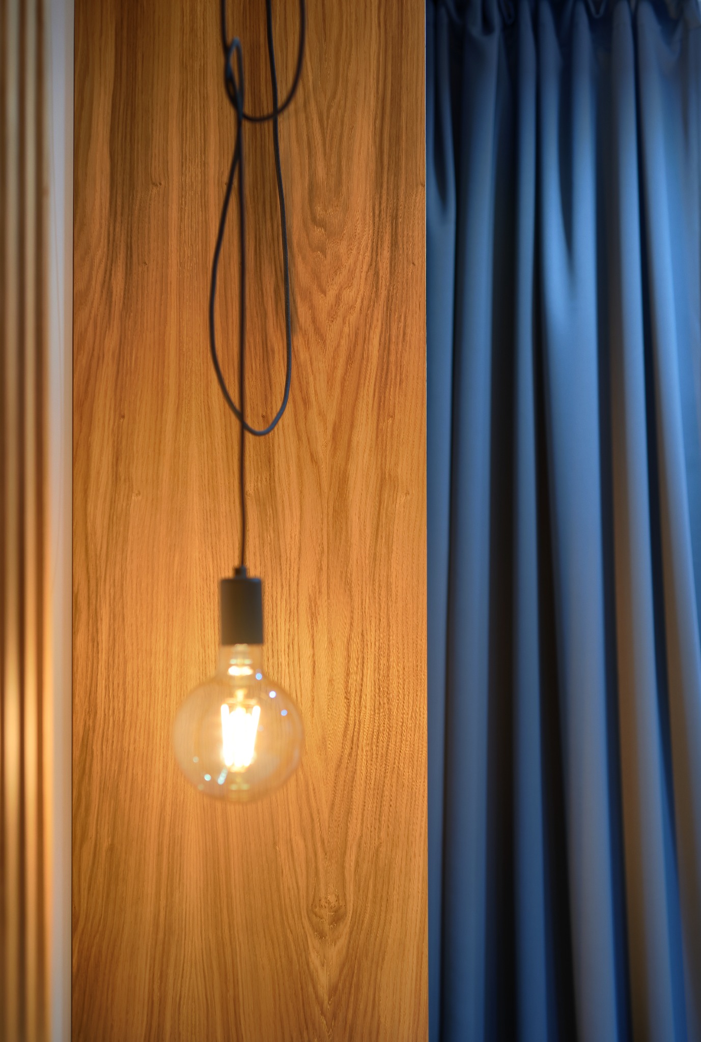 Żarówka Edisona na tle drewnianej ściany i zasłony, oświetlona ciepłym światłem.