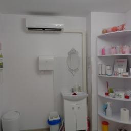 Cool-Install - Wnętrze gabinetu z klimatyzatorem na ścianie, umywalką z dekoracyjnym lustrem i półką narożną z kosmetykami.