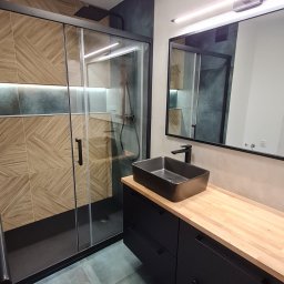 STYLOWE WNĘTRZE WARSZAWA MARIUSZ BIERNACKI - Nowoczesna łazienka z kabiną prysznicową typu walk-in, czarną armaturą i drewnianym blatem. Uwagę przykuwają geometryczne płytki na ścianie prysznica.