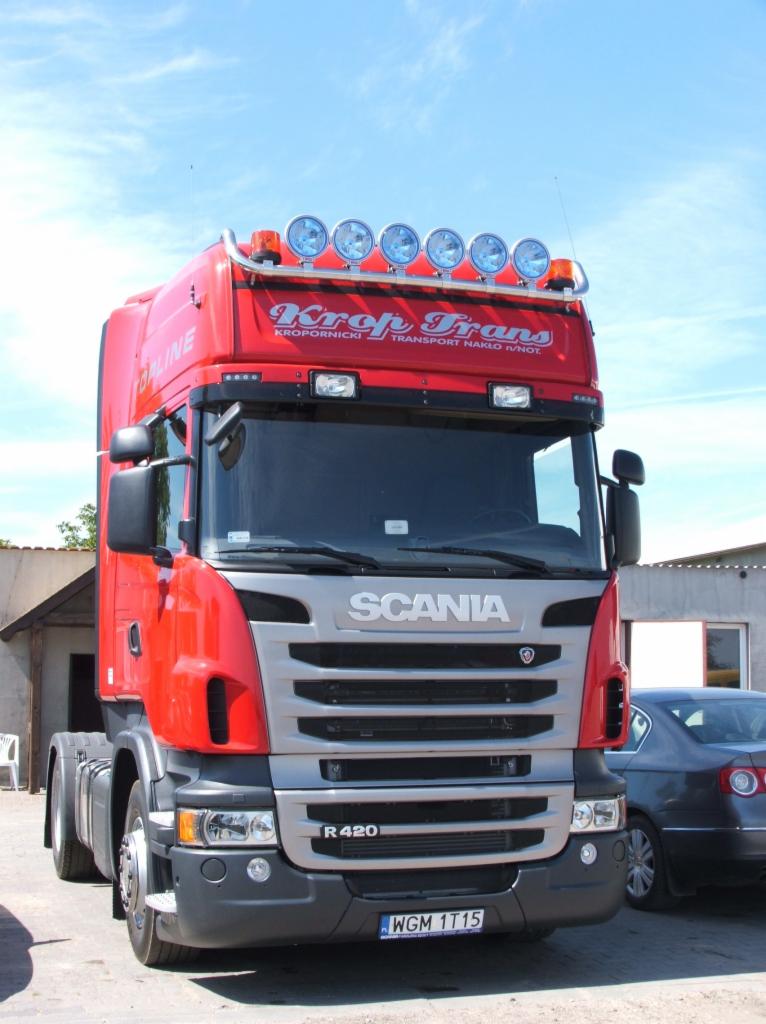 Czerwona ciężarówka Scania R420 firmy Krof-Trans z Nakła n/Not z sześcioma okrągłymi lampami na dachu, zaparkowana obok szarego samochodu osobowego.