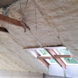 Termoprof Dawid Osiński - Poddasze ocieplone pianką PUR z widocznymi elementami drewnianej konstrukcji dachu, oknami dachowymi i zwisającymi przewodami.