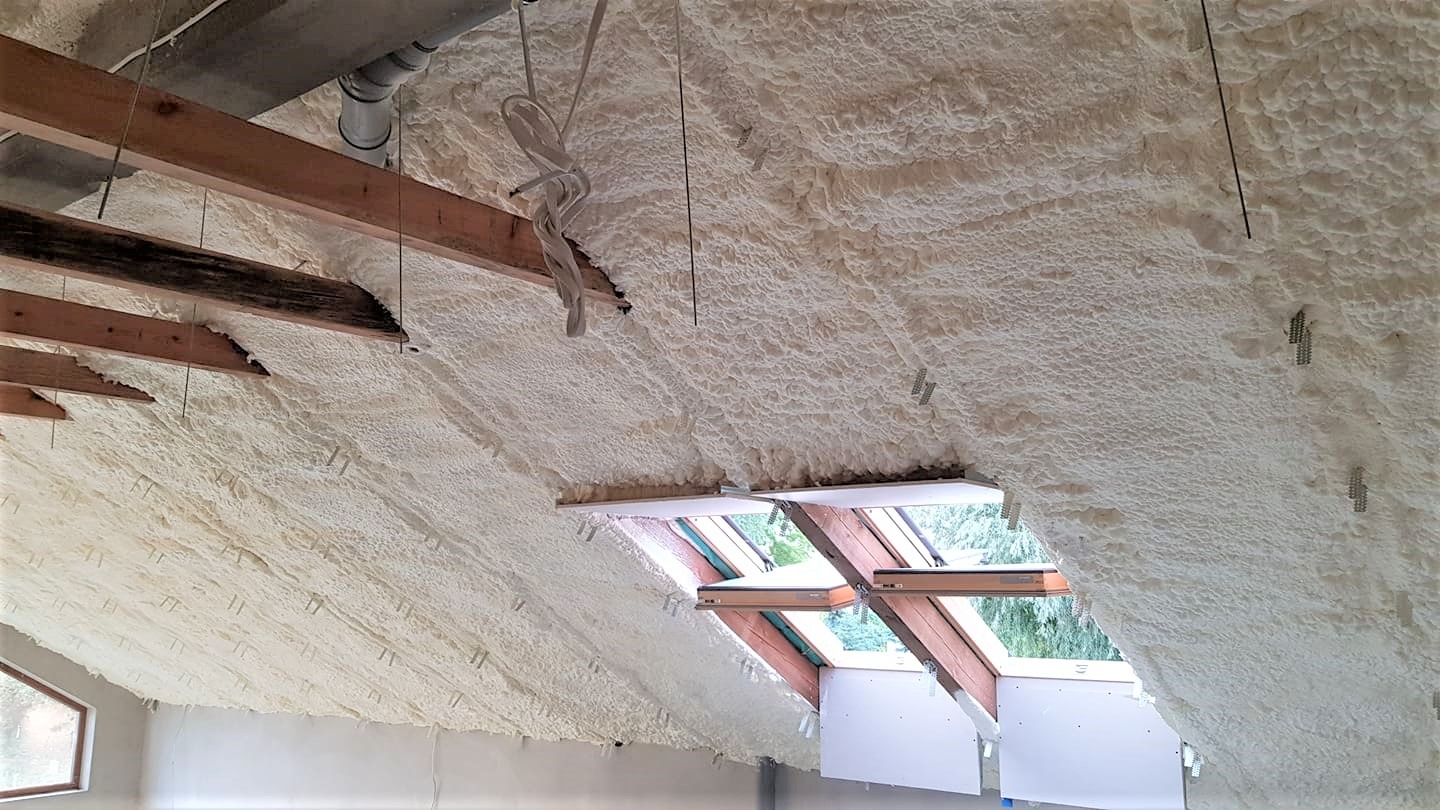 Poddasze ocieplone pianką PUR z widocznymi elementami drewnianej konstrukcji dachu, oknami dachowymi i zwisającymi przewodami.
