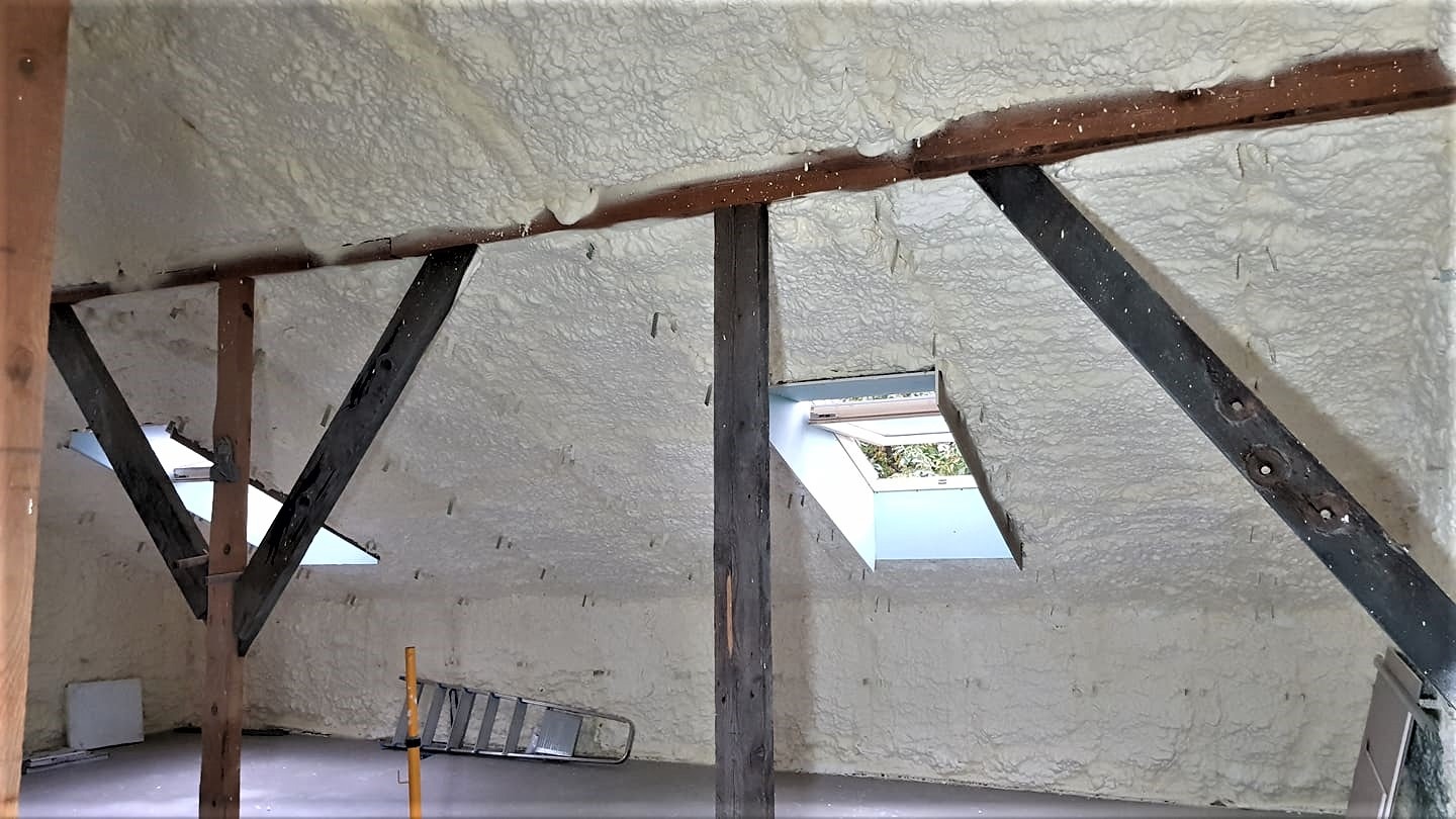 Poddasze po ociepleniu pianką, widoczne drewniane krokwie i okno dachowe, na podłodze drabina aluminiowa
