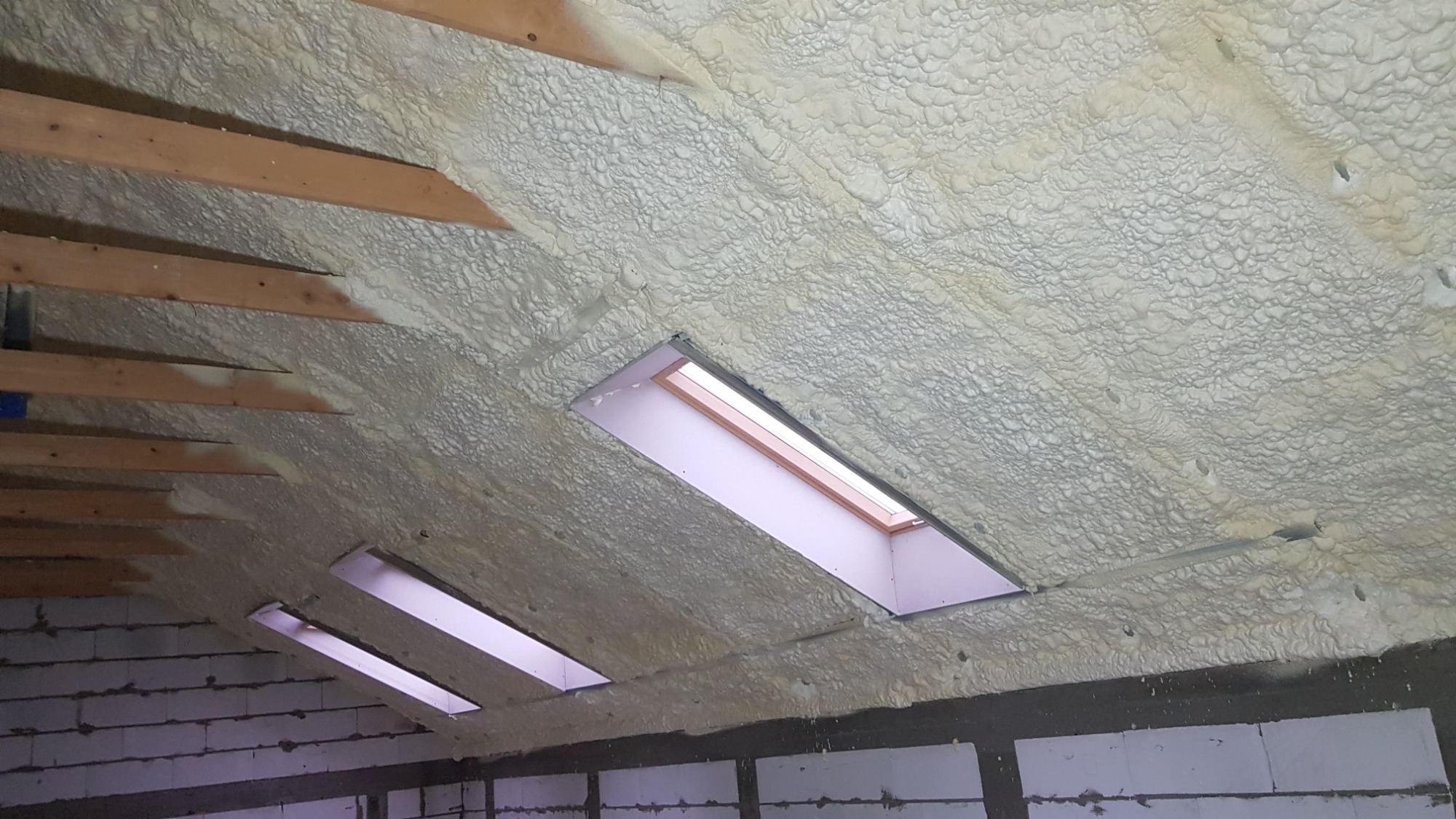 Poddasze w Tczowie po natrysku pianki poliuretanowej, widoczne drewniane belki i okna dachowe przed wykończeniem.