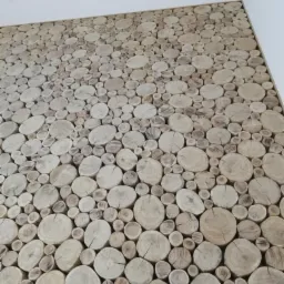 Dekoracyjna ściana wykończona okrągłymi plastrami drewna o różnej średnicy, tworząca naturalną mozaikę na białym tle sufitu.