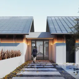 Kobieta wchodzi do nowoczesnego domu z dwuspadowym dachem, ścieżka z płyt betonowych usiana jesiennymi liśćmi, minimalistyczna elewacja z drewnianymi akcentami.