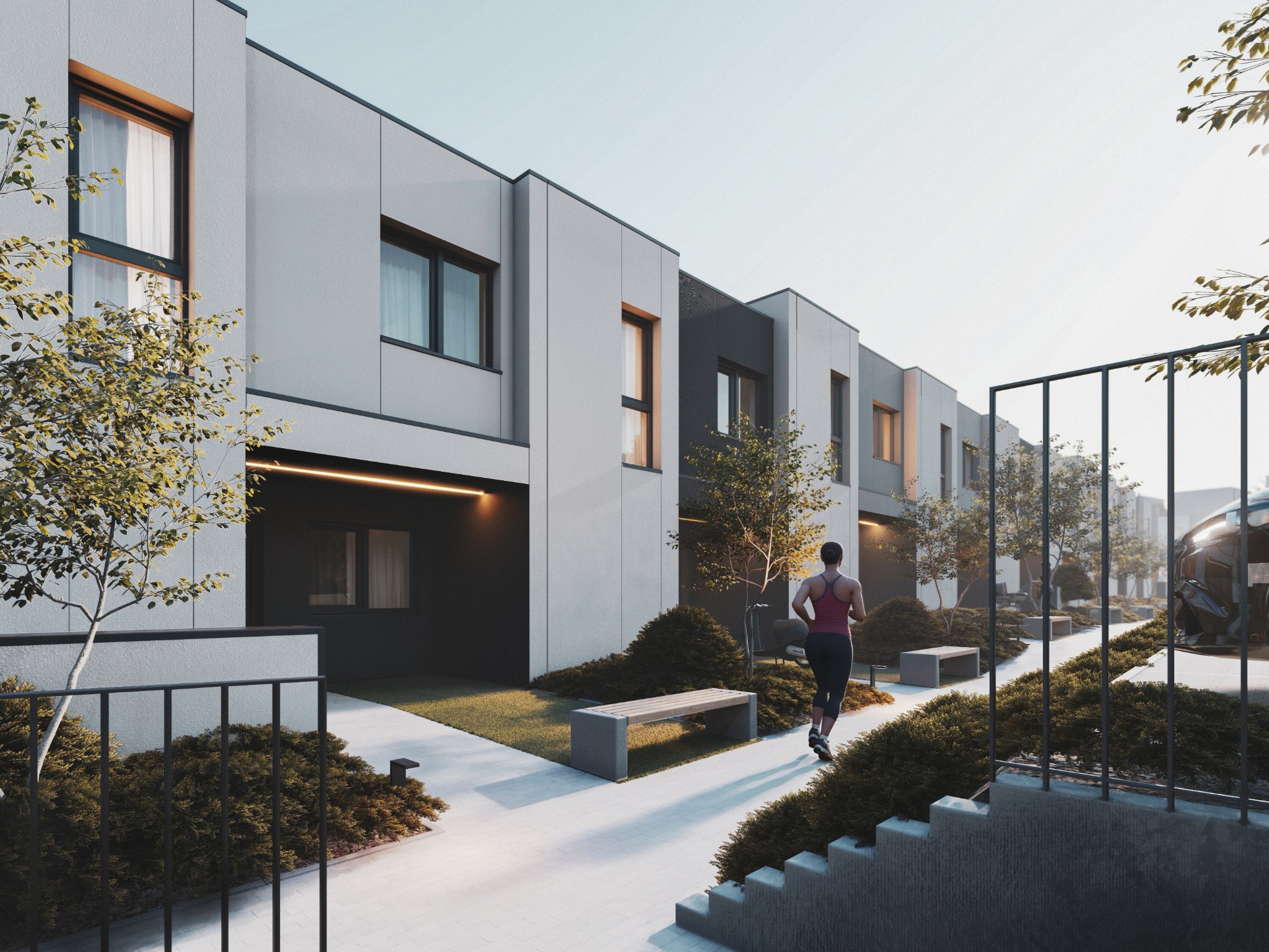 Nowoczesne szeregówki z minimalistyczną elewacją w odcieniach szarości, z zadbanym ogrodem i biegnącą osobą. Ujęcie z poziomu gruntu, podkreślające architekturę.