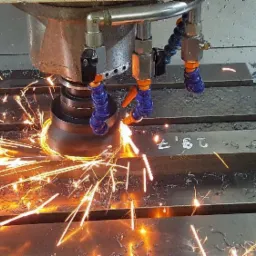 Metalowa obróbka skrawaniem z chłodziwem, widoczne iskry i wióry na stole roboczym z numerem '29,7'.