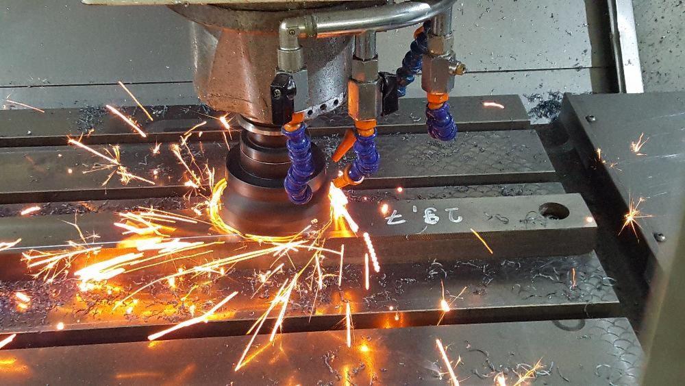 Metalowa obróbka skrawaniem z chłodziwem, widoczne iskry i wióry na stole roboczym z numerem '29,7'.