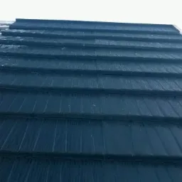 Fragment dachu pokrytego ciemną blachodachówką modułową, częściowo ośnieżonego, widok z dołu.