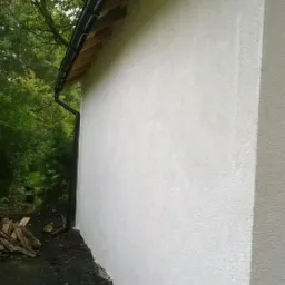 Świeżo otynkowana ściana zewnętrzna budynku z zamontowanym czarnym systemem rynnowym, widok z dołu.