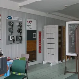 Ekspozycja w salonie: próbki profili okiennych, modele drzwi zewnętrzne i mechanizmy rolet nadstawnych na ścianie.