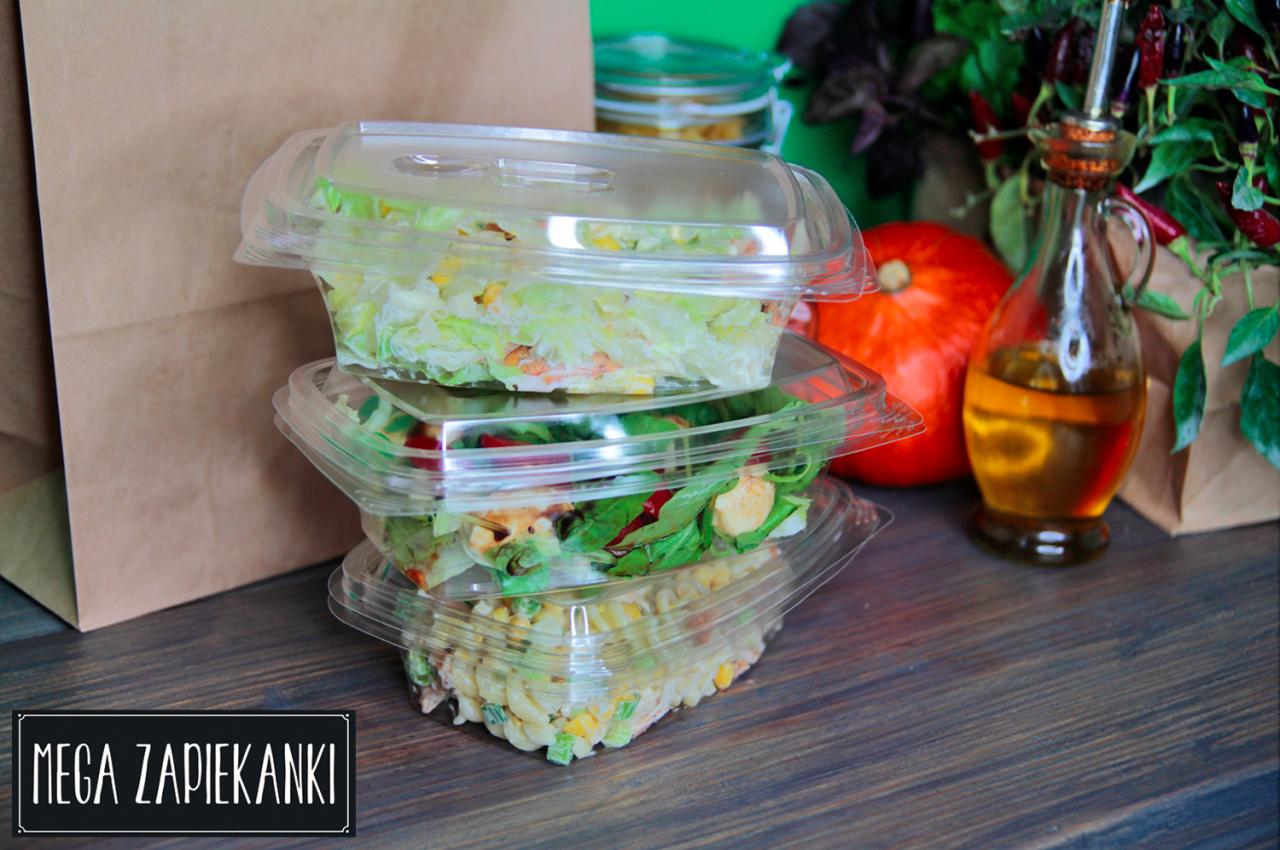 Stos trzech przezroczystych pojemników z różnymi sałatkami, widoczna dynia, butelka z oliwą i logo 'Mega Zapiekanki' w rogu.
