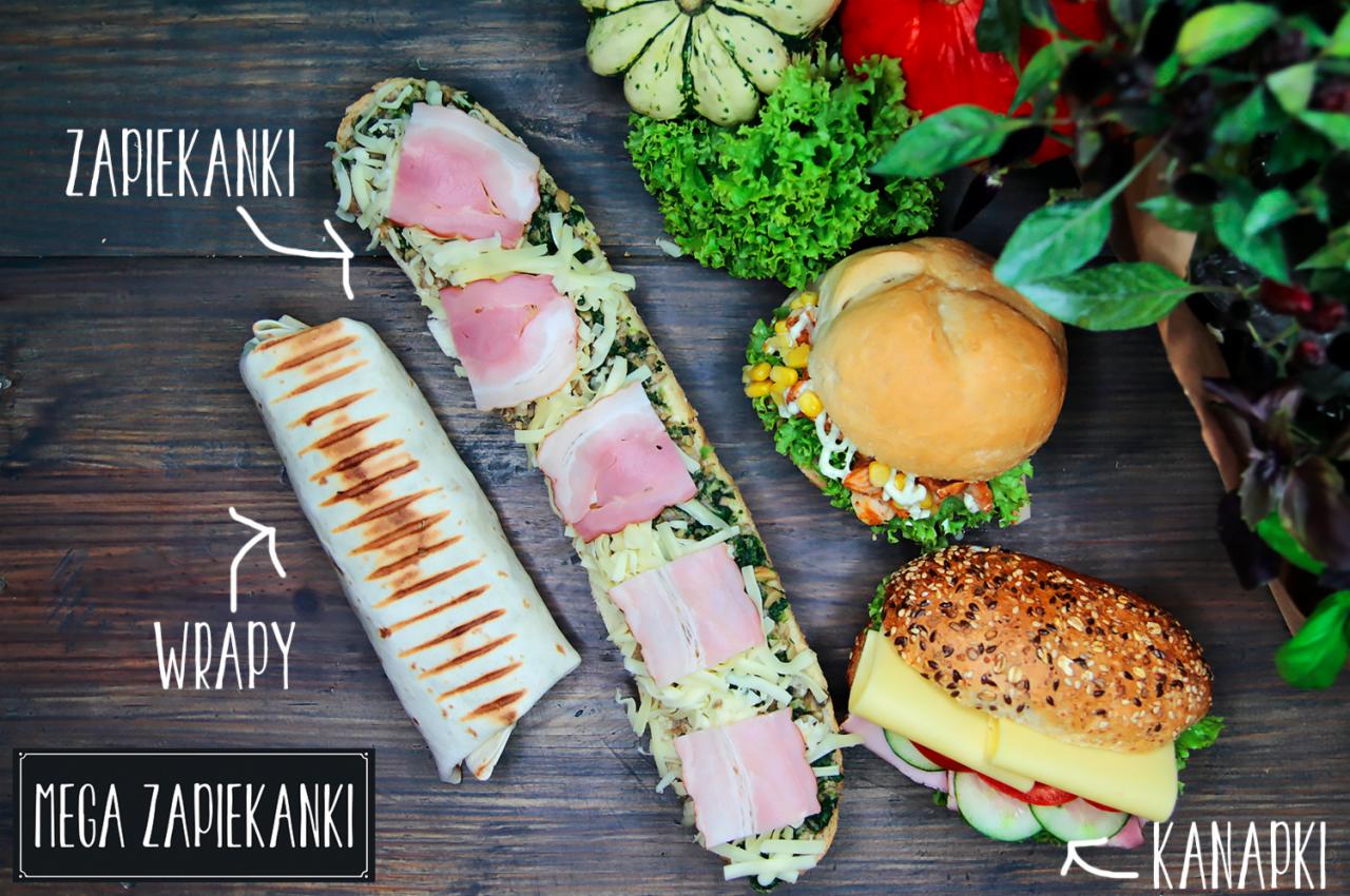 Widok z góry na drewniany stół z różnorodnym jedzeniem: wrap, zapiekanka z szynką, kanapki z warzywami i serem, dynie ozdobne i zielenina