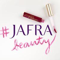 Błyszczyk do ust marki JAFRA w odcieniu burgundu, leżący obok napisu 'JAFRA beauty' wykonanego błyszczykiem na białym tle, z hashtagiem obok nazwy marki.