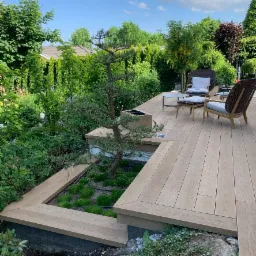 Jasny taras z drewna w Wejherowie, z wkomponowanym zielonym ogrodem z małym drzewkiem bonsai i kompletem mebli ogrodowych z wikliny.