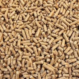 Jasne, brązowe granulki pelletu drzewnego ułożone gęsto, widoczne drobne pęknięcia i nierówności na powierzchni.