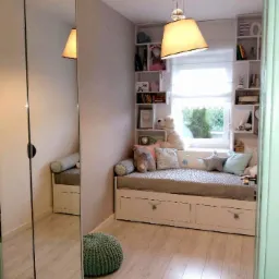 Pokój dziecięcy z łóżkiem wnękowym z szufladami, zabudowaną półką nad oknem i lustrzaną szafą przesuwną po lewej stronie, oświetlony wiszącą lampą.