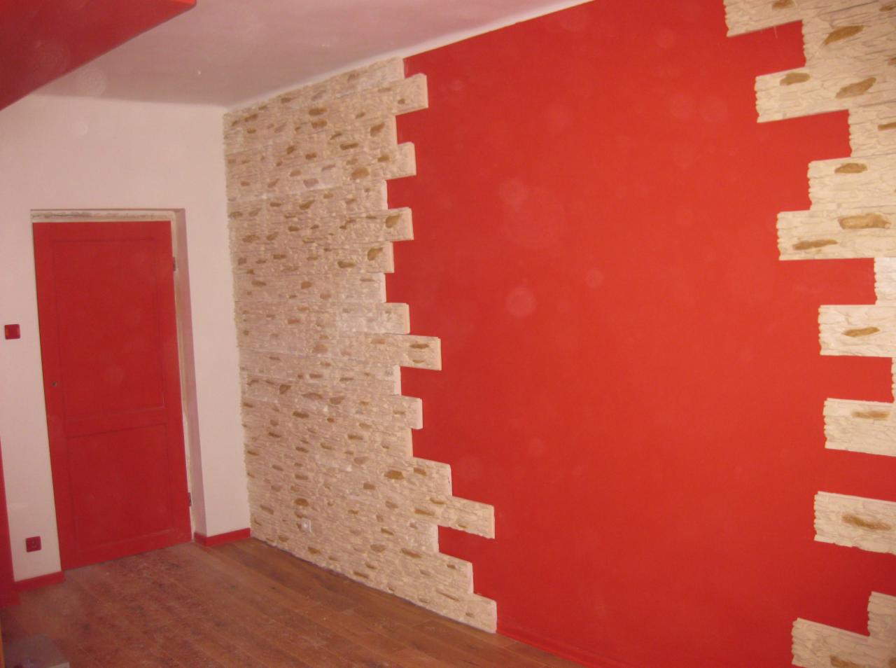 Częściowo wykończona ściana z dekoracyjną okładziną imitującą kamień, zestawiona z intensywnie czerwoną, pomalowaną powierzchnią, widoczna drewniana podłoga i czerwone drzwi w tle.