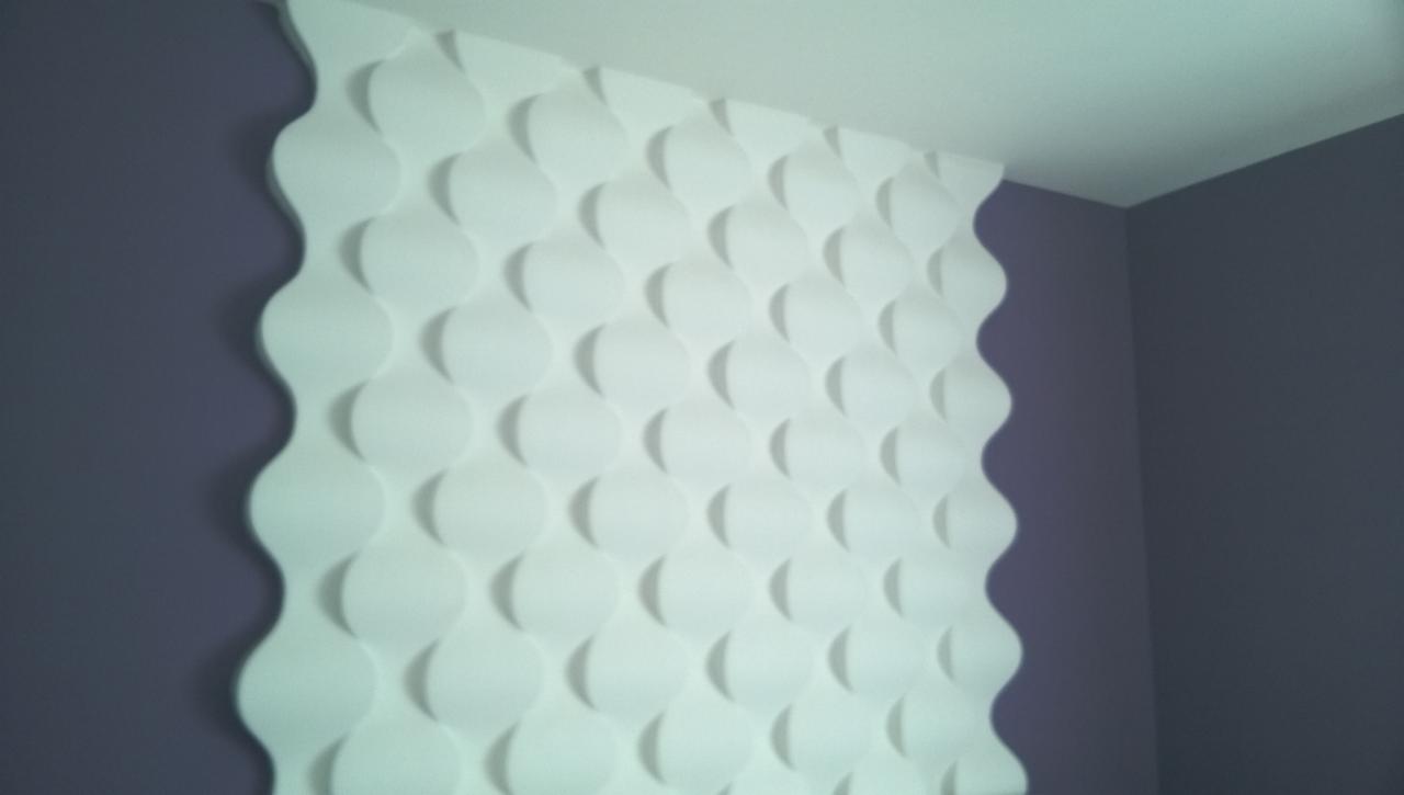 Biała, trójwymiarowa dekoracja ścienna z motywem falistych kół na fioletowej ścianie, widok pod kątem.