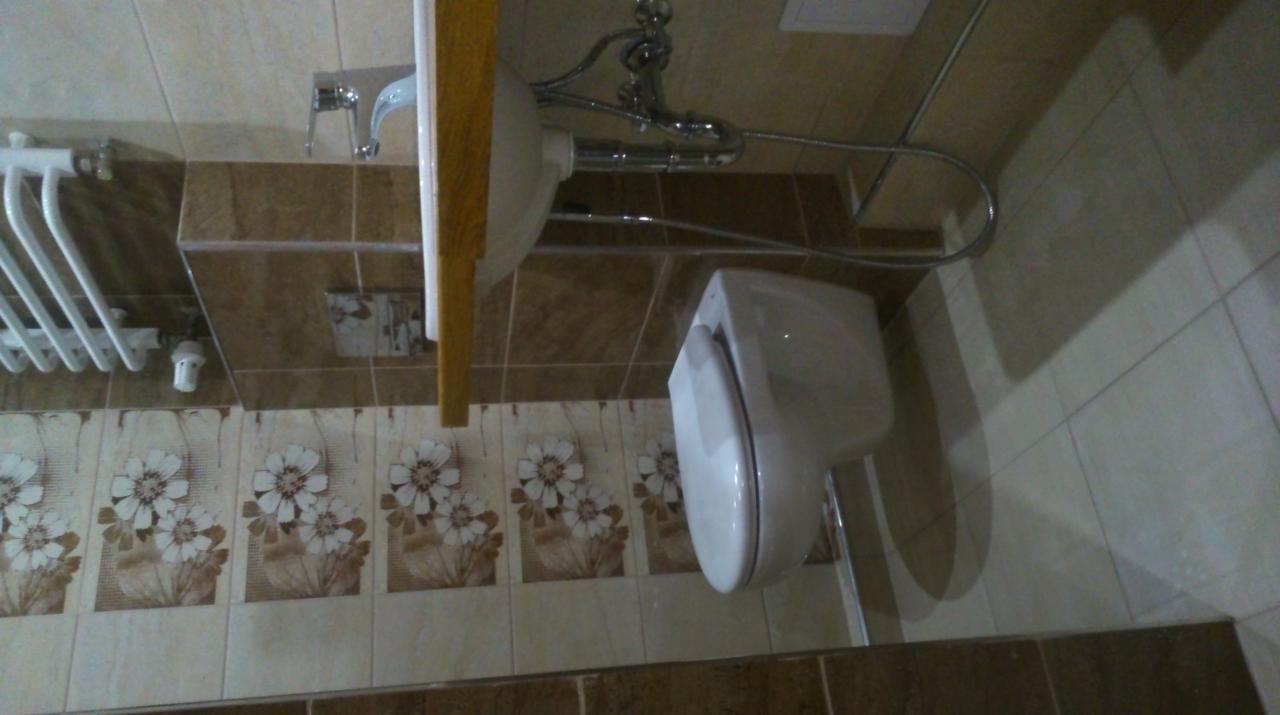 Ukończona łazienka z beżowymi płytkami z motywem kwiatowym, biała umywalka z chromowaną armaturą, grzejnik drabinkowy i podwieszana toaleta