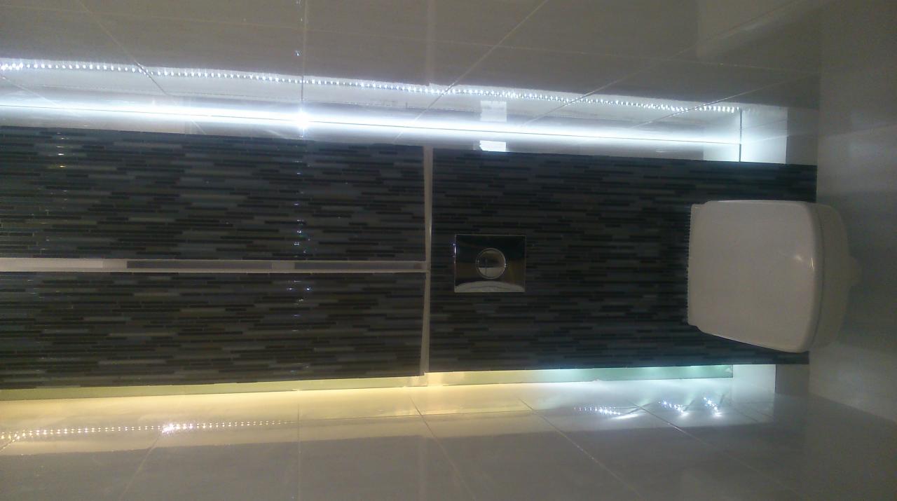 Nowoczesna toaleta podwieszana z mozaikową ścianą i podświetleniem LED na górze i dole, widoczny przycisk spłukiwania.