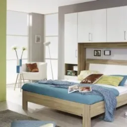 Nowoczesna sypialnia z łóżkiem i zabudową meblową z szafkami wiszącymi w kolorze białym i drewnopodobnym, z elementami otwartymi po bokach łóżka.