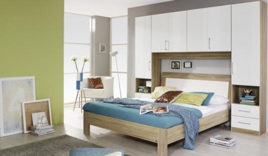 Nowoczesna sypialnia z łóżkiem i zabudową meblową z szafkami wiszącymi w kolorze białym i drewnopodobnym, z elementami otwartymi po bokach łóżka.