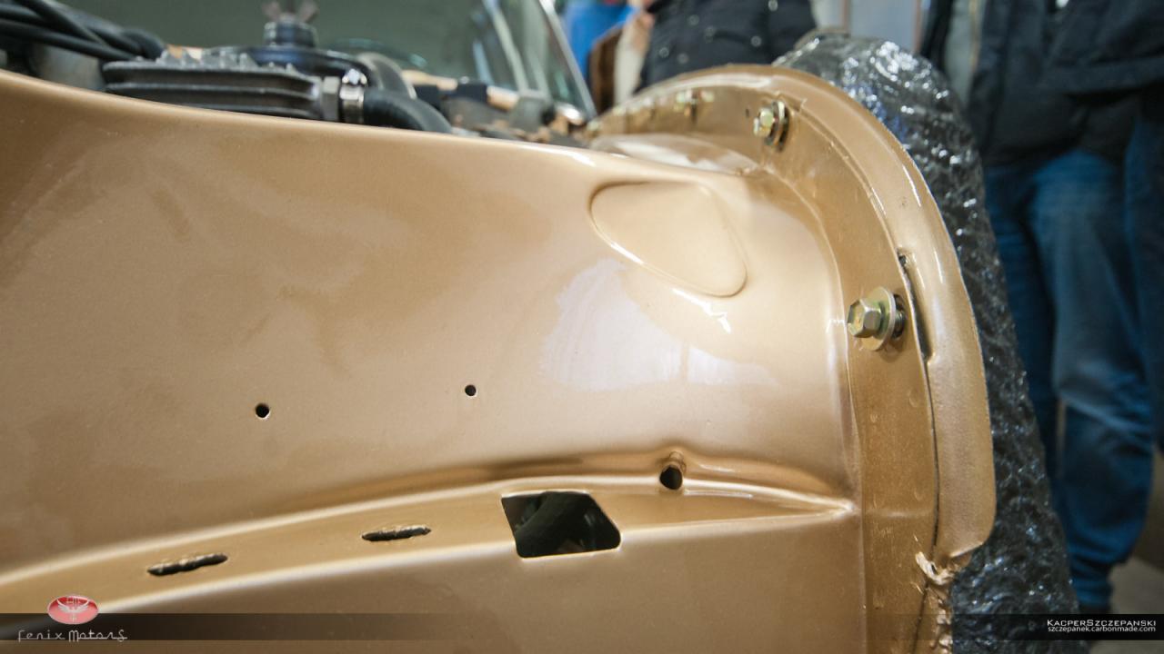 Złoty błotnik samochodu po naprawie, widoczne ślady szpachlowania i przygotowania do lakierowania, z zamontowanymi śrubami mocującymi.