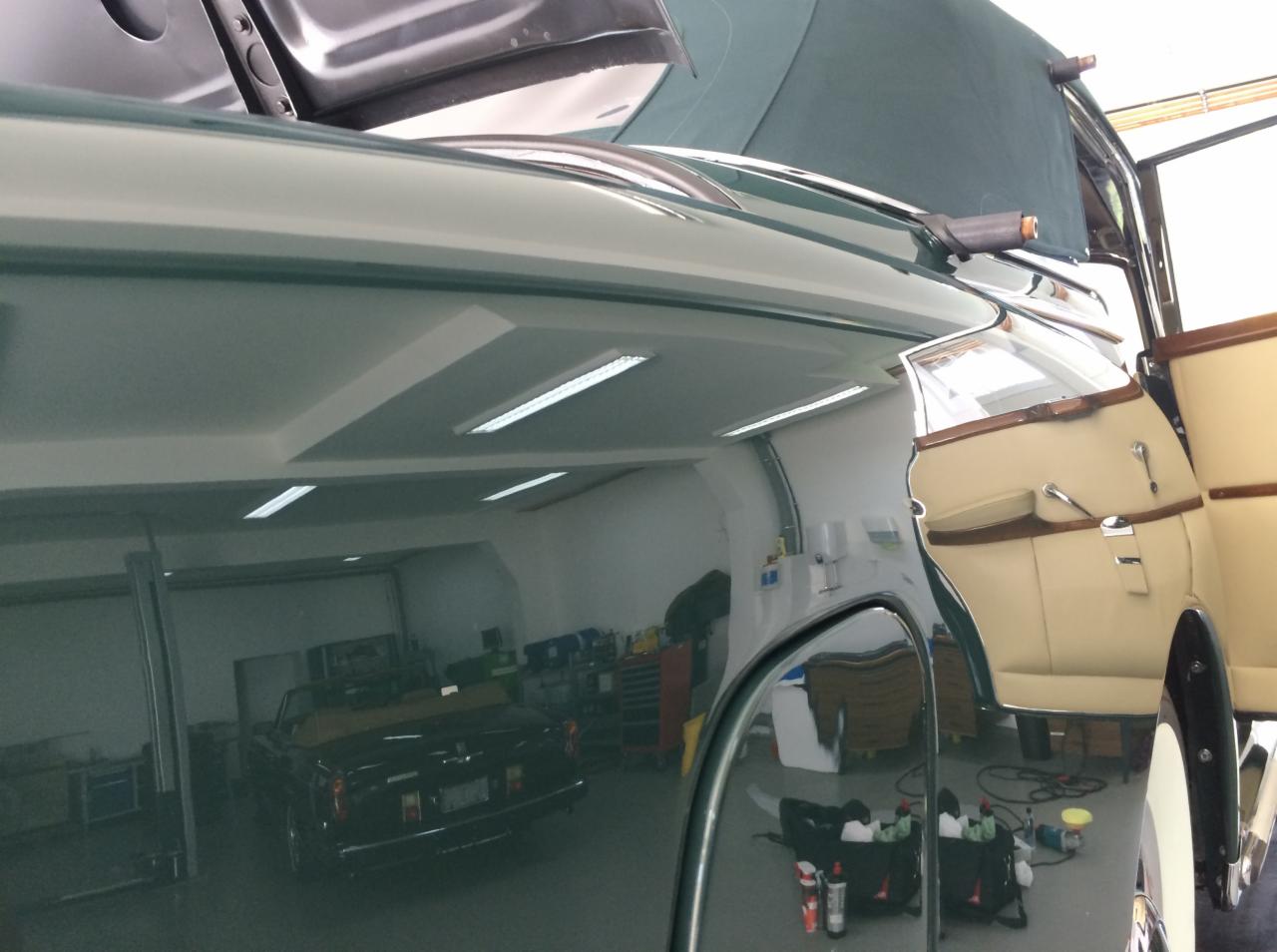 Błyszczący, zielony lakier klasycznego kabrioletu po renowacji w warsztacie w Hornówku, z widocznym odbiciem wnętrza warsztatu i zaparkowanego innego auta. Otwarte drzwi ukazują beżową tapicerkę.
