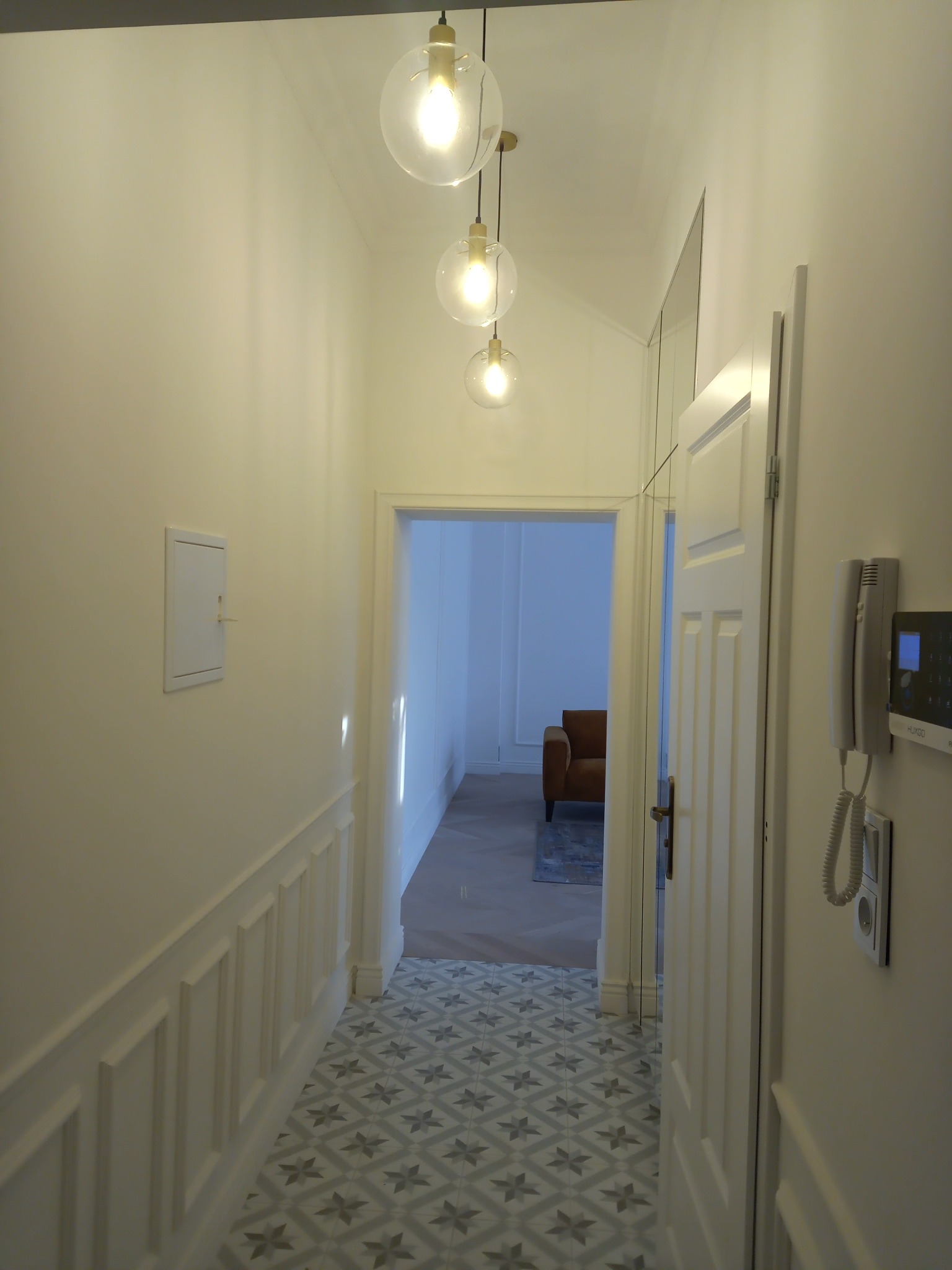 Korytarz po remoncie z dekoracyjną listwą przypodłogową, wzorzystą podłogą i trzema szklanymi lampami wiszącymi.