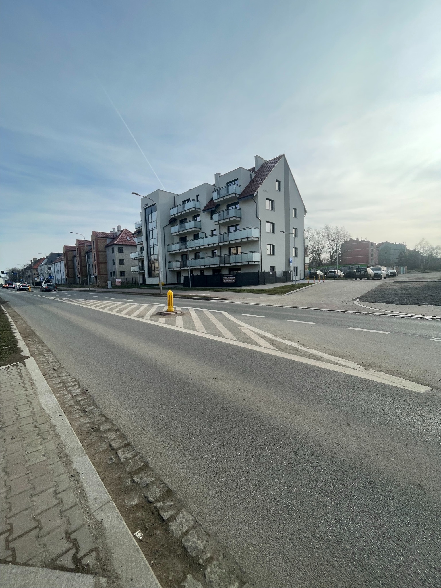 Nowoczesny budynek wielorodzinny z balkonami we Wrocławiu, widok z perspektywy ulicy w słoneczny dzień.