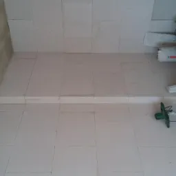 Świeżo wyłożona, biała podłoga z płyt kartonowo-gipsowych w pomieszczeniu, widoczne narzędzia i materiały budowlane, ściana w trakcie przygotowywania pod gładź.