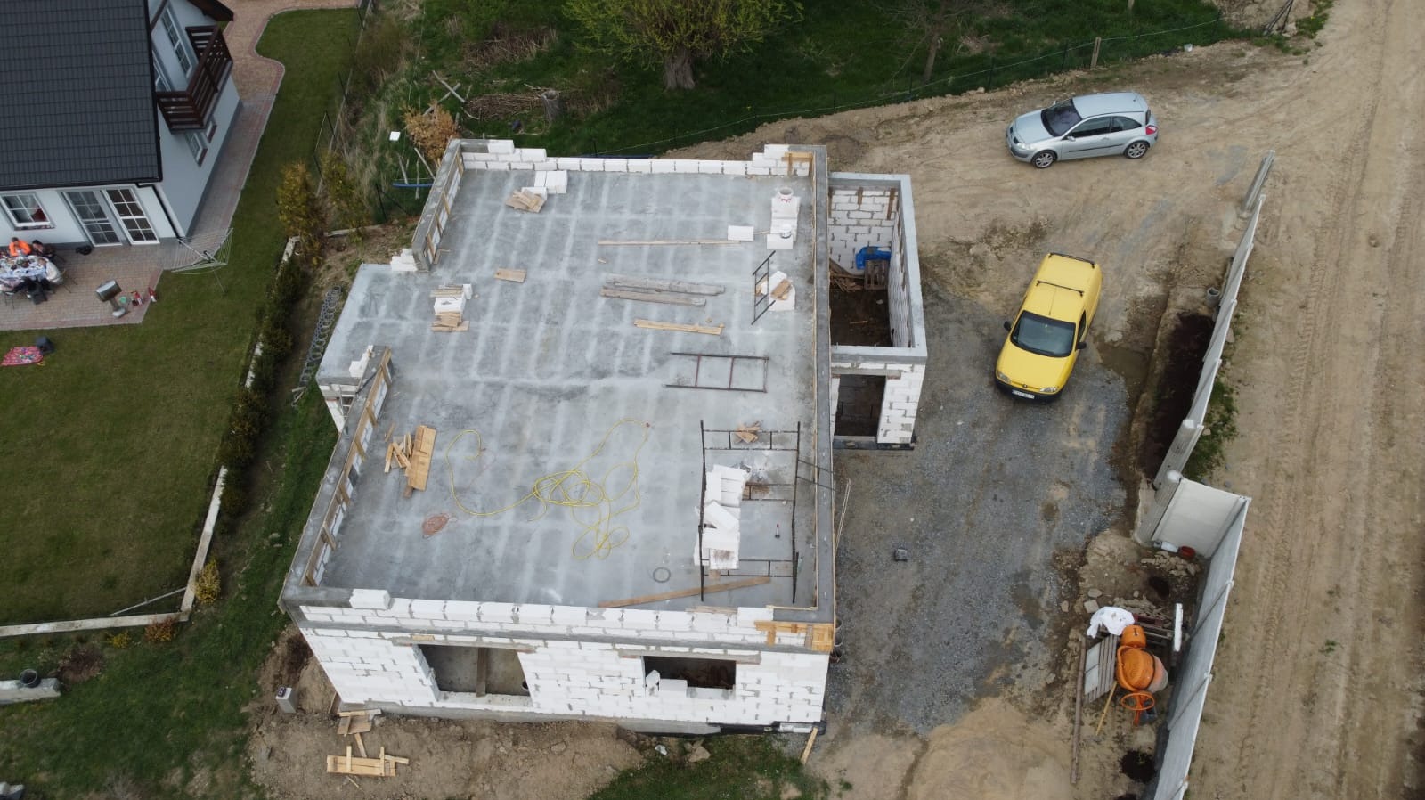 Budowa domu jednorodzinnego z betonu komórkowego, widok z góry. Wylany fundament, częściowo wymurowane ściany. Na posesji zaparkowane dwa samochody.