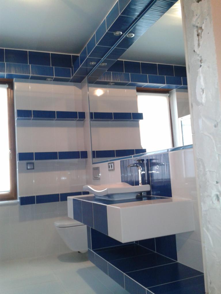 Nowoczesna łazienka z białymi i niebieskimi płytkami, umywalką nablatową i toaletą w zabudowie, widok na fragment ściany w trakcie wykończenia.