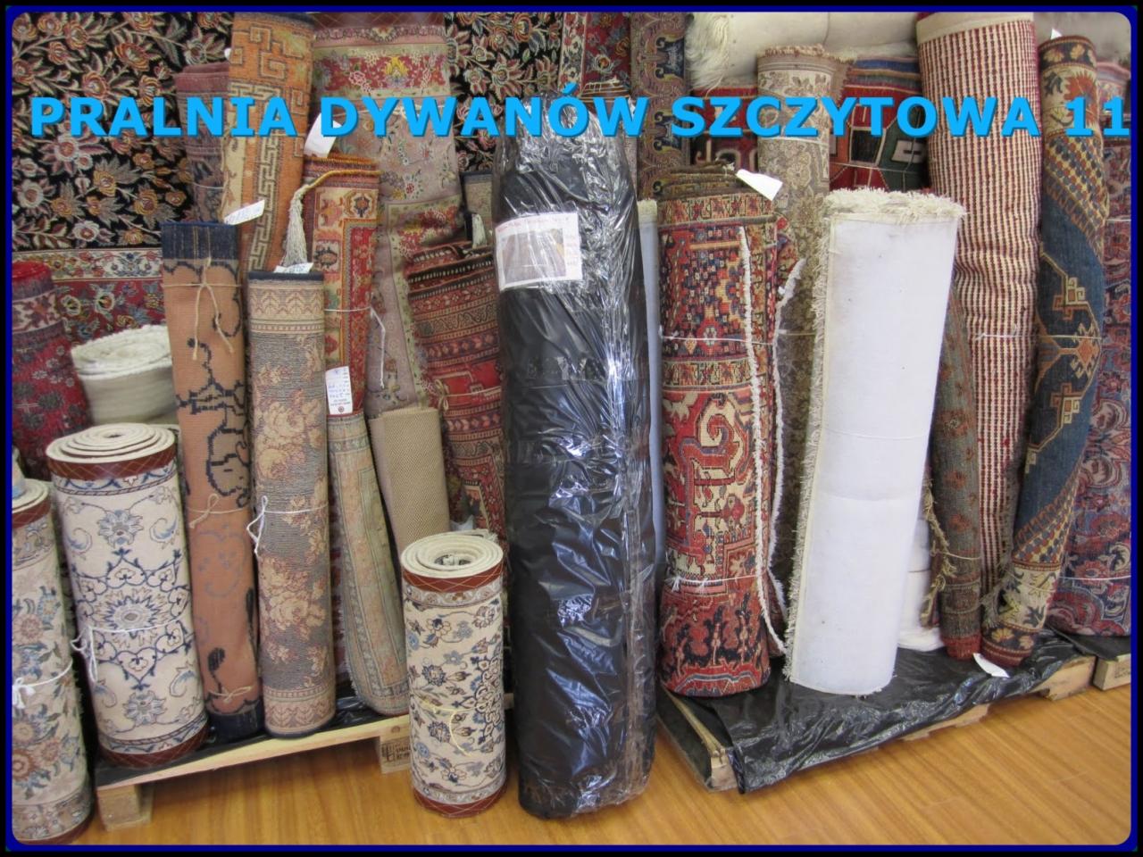 Stos zwiniętych dywanów w pralni, niektóre zapakowane w folię, widoczne różnorodne wzory i kolory, na drewnianej palecie.