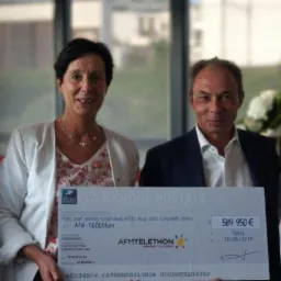 Cztery osoby prezentują czek La Banque Postale dla AFM-Téléthon na kwotę 589 950 euro, z datą 18/06/2019, w tle widoczne kwiaty.