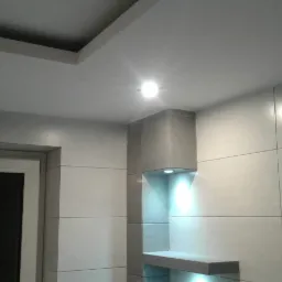 Wykończona łazienka z szarymi płytkami wielkoformatowymi, podświetlana półka w zabudowie, sufit podwieszany z oświetleniem punktowym.