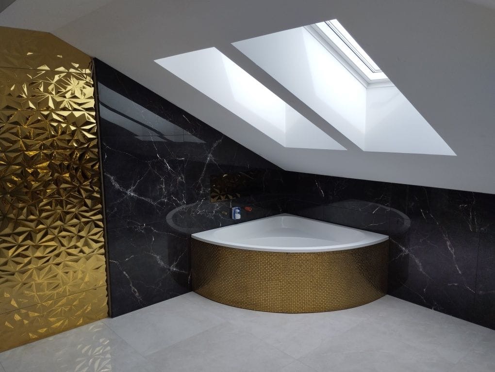 Nowoczesna łazienka na poddaszu z narożną wanną obudowaną mozaiką, ściany wyłożone czarnym marmurem i złotą, trójwymiarową płytką, trzy okna dachowe w skosie.