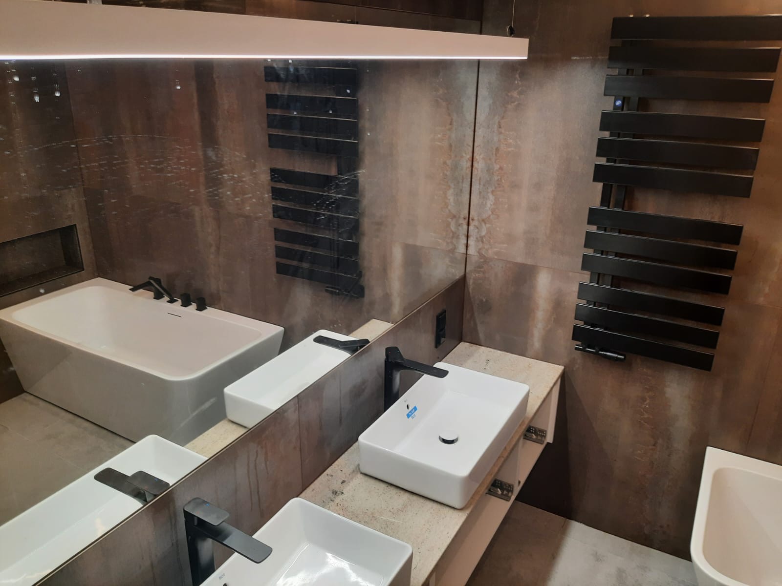 Nowoczesna łazienka w Kaarst z wanną, umywalkami nablatowymi i grzejnikiem drabinkowym na tle ściany z efektem rdzy, odbijająca się w lustrze.