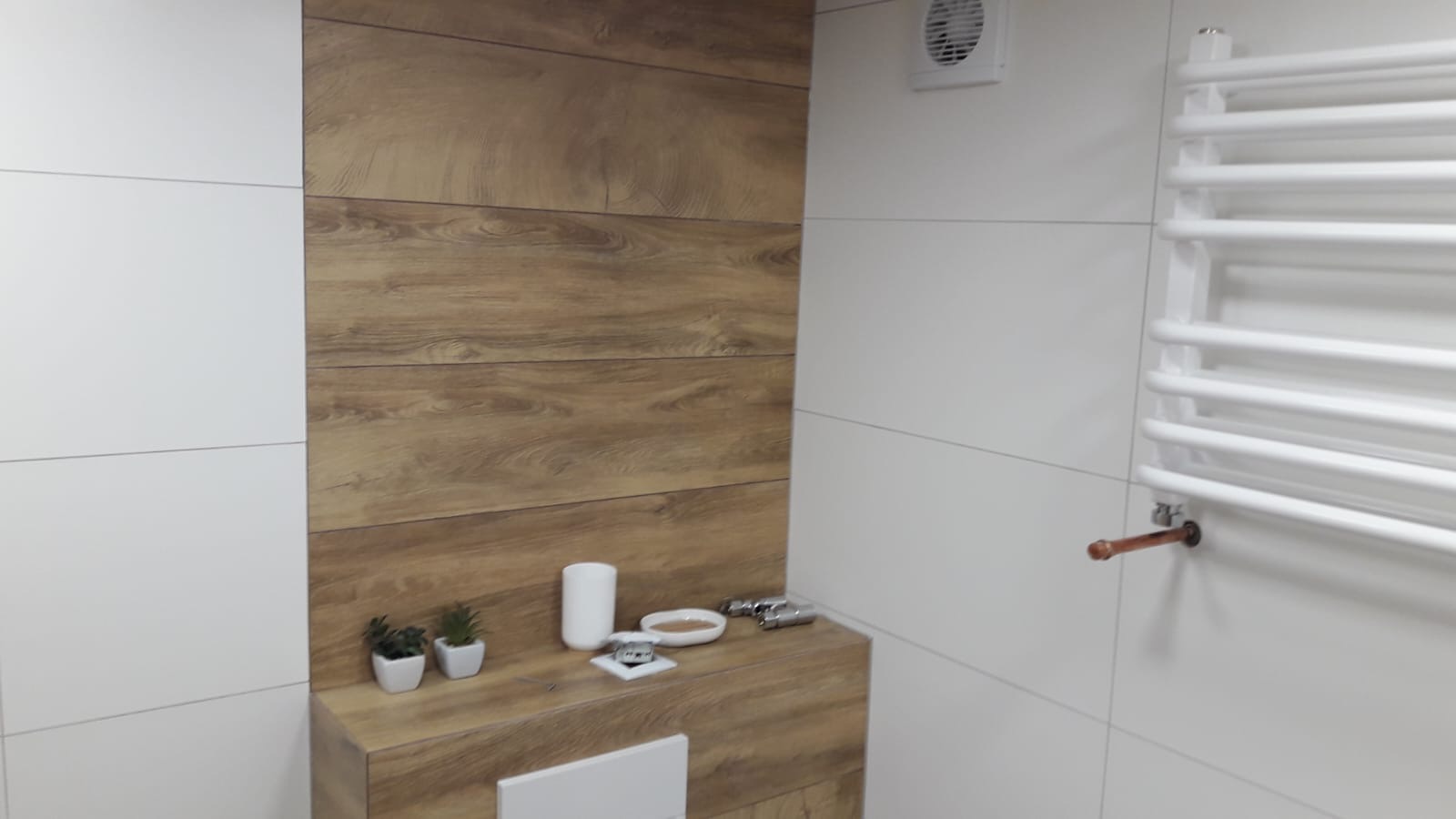 Nowoczesna łazienka z białymi i drewnopodobnymi płytkami, grzejnikiem drabinkowym i drewnianym blatem z dekoracjami.